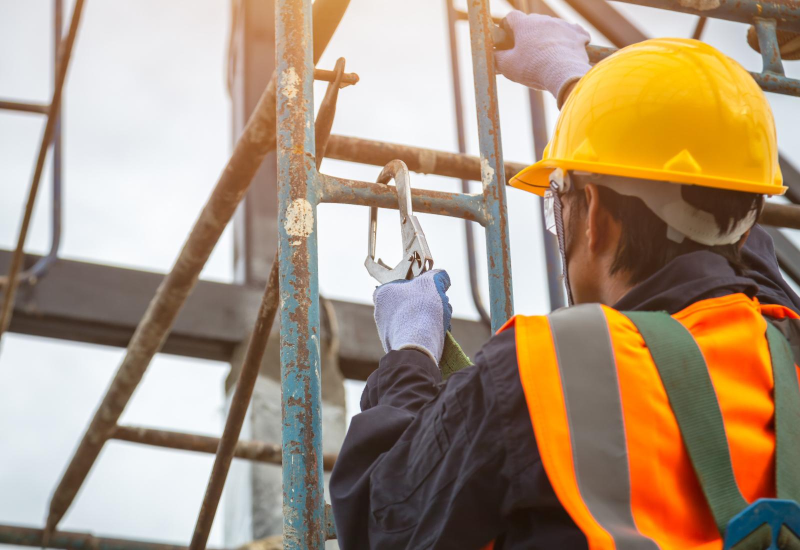 A person in a hard hat and safety vest attaches a metal clip to scaffolding.